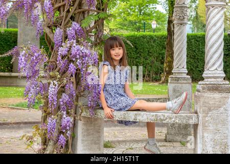 Sieben Jahre altes Mädchen, das in Honfleur, Frankreich, unter einem Glyzinienbaum sitzt Stockfoto