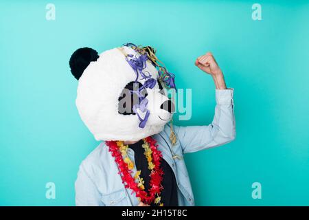 Aufgeregter Mann in Panda-Maske mit Party-Ornamenten auf farbigem Hintergrund Stockfoto