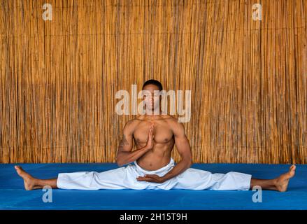 Afrikanische Männer, die bei einem Dojo, einem Wettkampftraining, auf einem blauen Boden eine Spaltung durchmachen Stockfoto