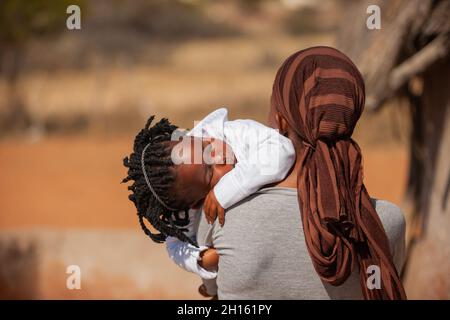 Afrikanische Frau in einem Dorf in Botswana trägt ihre Tochter schlafend Stockfoto