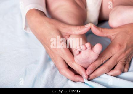 Kinderfüße in herzförmigen Händen der Mutter. Schönes konzeptuelles Bild der Mutterschaft Stockfoto