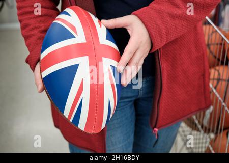 Frau in einem Geschäft kauft Rugby und American Football Ball mit Druck der britischen Flagge Stockfoto