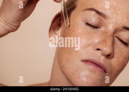 Junge schöne Frau mit geschlossenen Augen, die Gesichtsserum mit Pipette aufbringen Stockfoto