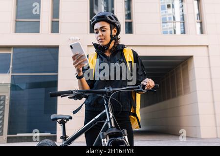 Kurier mit Fahrrad liefert Essen. Junger Kurier, der die Lieferadresse auf dem Smartphone überprüft. Stockfoto