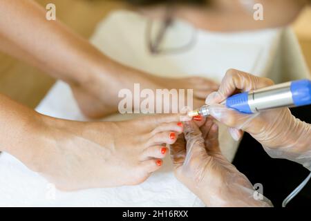 Kosmetikerin, die eine Pediküre malt, um die Nägel ihrer Kundin in einem Beauty-Center zu malen. Stockfoto