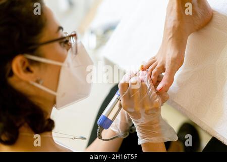 Kosmetikerin, die eine Pediküre malt, um die Nägel ihrer Kundin in einem Beauty-Center zu malen. Stockfoto