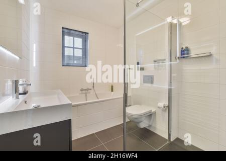 Waschbecken und Toilette befinden sich in der Nähe der Badewanne hinter einer Glaswand in einem hellen Badezimmer zu Hause Stockfoto