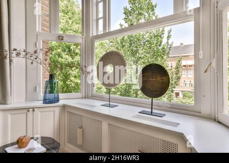 Runde Dekorationen und Zweige in Glasvase auf Fensterbank im hellen Raum der modernen Wohnung platziert Stockfoto