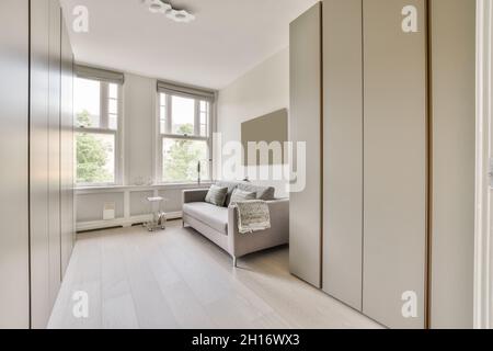 Komfortables Sofa mit Kissen und minimalistischen Schränken in der Nähe der Fenster im sonnendurchfluteten Wohnzimmer Stockfoto