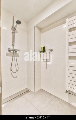 Modernes Badezimmer mit Dusche gegen Regal mit Flaschen an der gefliesten Wand im hellen Haus Stockfoto