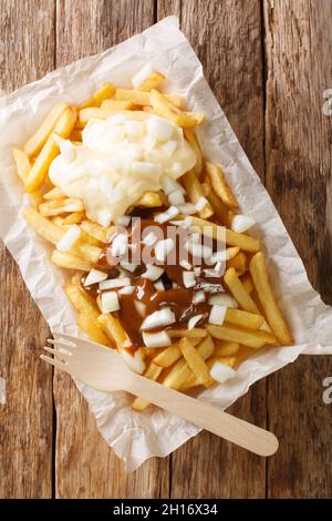 Patatje Oorlog Dutch war Fries gekrönt mit Mayonnaise, einer dicken Erdnusssauce im indonesischen Stil, und rohen Zwiebeln in der Nähe auf dem Teller auf dem Tisch. Vertica Stockfoto