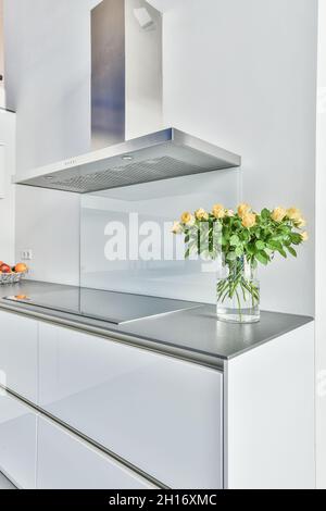 Kreatives Design der Küche mit Kapuze über dem Elektroherd gegen blühenden Blumenstrauß in Vase auf dem Tisch zu Hause Stockfoto