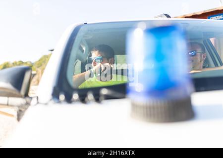 Seitenansicht des Rettungsschwimmers in einer Sonnenbrille, der das Auto in der Nähe eines Mannes fährt, der während des Arbeitstages mit dem Funkgerät spricht Stockfoto