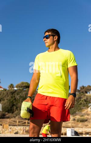 Mann Rettungsschwimmer in Shorts und T-Shirt und Aufrechterhaltung der Sicherheit an der sandigen Küste Stockfoto