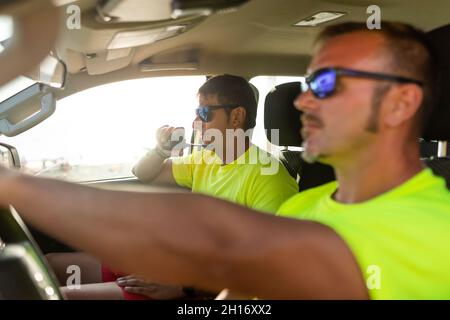 Seitenansicht des Rettungsschwimmers in einer Sonnenbrille, der das Auto in der Nähe eines Mannes fährt, der während des Arbeitstages mit dem Funkgerät spricht Stockfoto