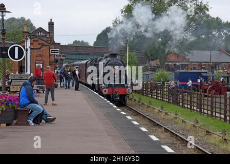 Eisenbahnliebhaber, die die ehemalige Dampflokomotive „8F“ der LMS 48305 beobachten, kommen an der Station Quorn & Woodhouse der Great Central Heritage Railway in Leicestershire an Stockfoto