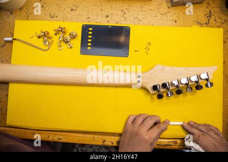 Draufsicht auf Crop anonymen männlichen Geigenbauer am Tisch mit hölzernen E-Gitarre Hals mit Metall-Stimmschlüssel in der Werkstatt Stockfoto