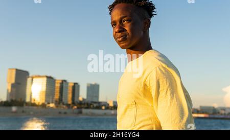 Durch ein Glas positiver indischer Frau, die den Zucker in einer Tasse heißen Kaffees steuert, während sie in der modernen Cafeteria am Tisch sitzt Stockfoto