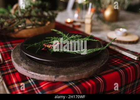 Von oben weihnachtliche Tischeinstellung mit Kranz auf Keramikplatte auf rot karierter Tischdecke auf dem Hintergrund Stockfoto