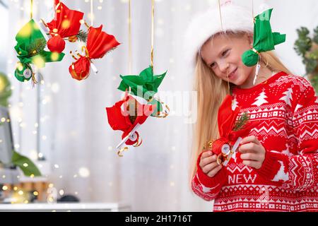 Kind Mädchen Eröffnung kleine Geschenke Überraschungen Adventskalender an der Wand hängen. Frohe Weihnachten und Neujahr. Stockfoto