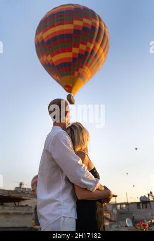 Niedriger Winkel von anonymen umarmen Paar auf der Straße stehen und Blick auf Heißluftballons schweben am Abend wolkenlosen Himmel Stockfoto