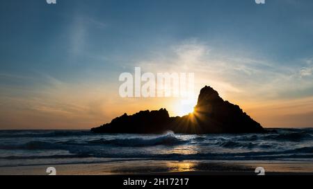 Karekare Strand bei Sonnenuntergang mit Sonnenstrahlen durch Panatahi Island, Waitakere, Auckland. Stockfoto