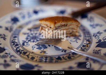 Leckere, süß gebackene Pfannkuchen auf weißem und blauem Teller mit Gabel, die bei Tageslicht auf den Tisch gelegt wird Stockfoto