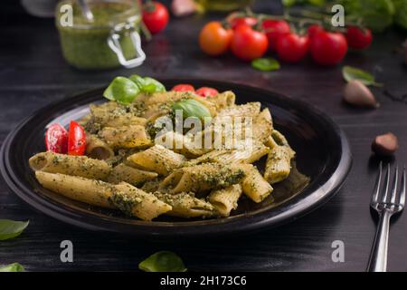 Von oben Teller mit leckeren Nudeln mit grüner Pesto-Sauce und Tomaten auf schwarzem Holztisch serviert Stockfoto