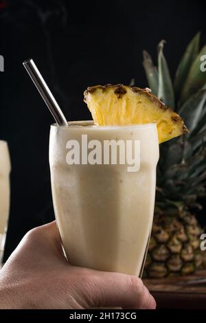 Ernte nicht erkennbare Person mit einem Glas Pina Colada Smoothie bestehend aus Ananassaft und Kokosnuss serviert mit wiederverwendbarem Stroh Stockfoto