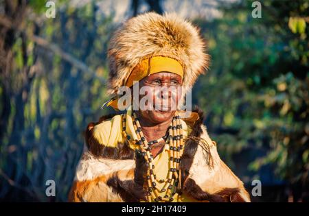 Zwei ältere Frauen aus dem südlichen Afrika, die in einer traditionellen Tracht mit Hut und Kuh gekleidet sind, verstecken sich in einem Dorf auf dem Land Stockfoto