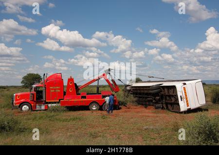 Abschleppwagen, der einen umgedrehten Bus am Straßenrand in den Busch hebt Stockfoto