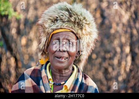 Zwei ältere Frauen aus dem südlichen Afrika, die in einer traditionellen Tracht mit Hut und Kuh gekleidet sind, verstecken sich in einem Dorf auf dem Land Stockfoto