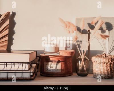 Gemütliches Herbsthaus Stillleben von trockenen Blumen in Vase, Strohdose, Glaskerze auf Holztisch und Schatten an der Wand von der hellen untergehenden Sonne. Kopieren Stockfoto