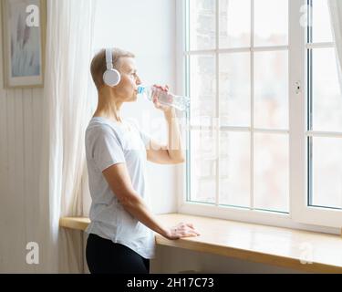Glückliche ältere Frau, die nach dem Sporttraining Wasser aus der Plastikflasche trinkt Stockfoto