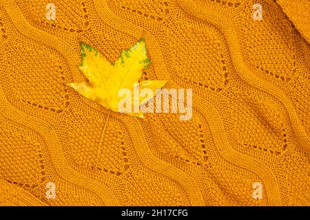 Ein leuchtend gelbes Blatt liegt auf dem Pullover. Herbstkomposition. Von oben gefilmt. Stockfoto