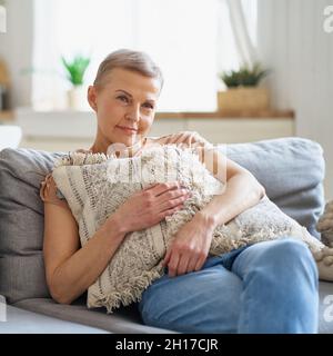 Glückliche Frau mittleren Alters, die zu Hause auf dem Sofa sitzt und fernsieht Stockfoto