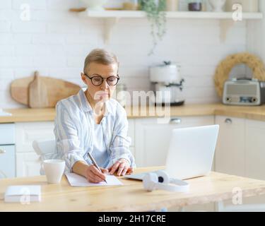 Konzentrierte ältere Schriftstellerin, die etwas auf dem Laptop tippt, während sie von zu Hause aus online arbeitet Stockfoto