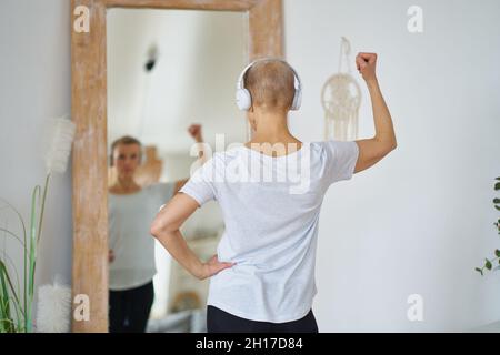 Sportliche ältere Frau, die sich im Spiegel vor einem großen Spiegel in der Wohnung des Hauses bewundert Stockfoto