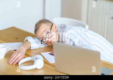 Reife Frau, die zu Hause in der Küche auf dem Tisch schläft, eine Pause macht, während sie arbeitet oder online studiert Stockfoto