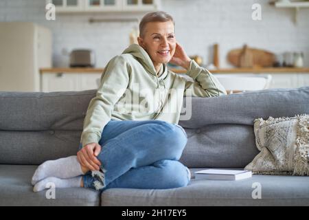 Schöne reife Frau in legerer Kleidung träumen von etwas, während Sie sich auf dem Sofa zu Hause entspannen Stockfoto
