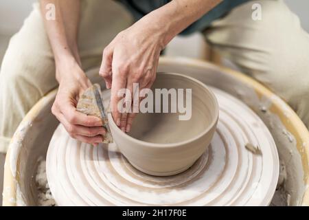 Nahaufnahme Frau Hände machen Tontopf in der Werkstatt. Unerkannte Künstler, die im Atelier aus nassem Ton modellieren. Unbekannte weibliche Keramikerin, die handgemachtes Produkt macht Stockfoto