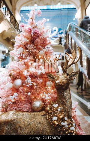 Goldener Hirsch, der in der Nähe des rosa Weihnachtsbaums steht. Festliche Dekorationen im Innenraum zum Neujahrsfest. Magische Atmosphäre Stockfoto