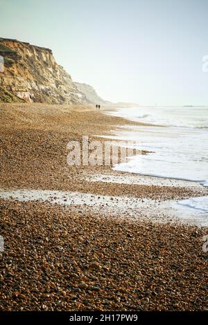 Zwei Personen, die im Winter in Großbritannien auf dem Hengistbury Head mit Cliffs an Einem Shingle Beach spazieren Stockfoto