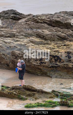 Ein Großvater mit seiner Enkelin, der bei Ebbe die Gezeitenzone am Fistral Beach in Newquay in Cornwall erkundet. Stockfoto