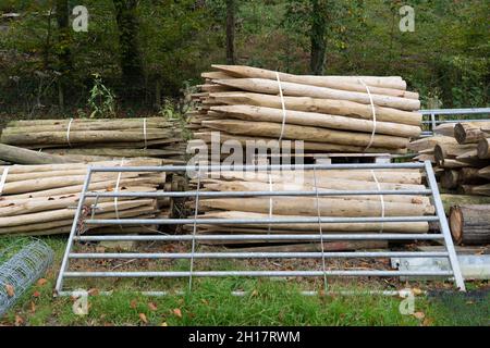 Bündeln von hölzernen Zaunpfosten, runden Holzpfählen und verzinktem Metalltor Stockfoto