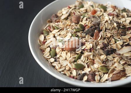 Frühstück Hafermüsli mit Nüssen, Samen und getrockneten Früchten in einer weißen Schüssel auf dunklem Grund. Stockfoto