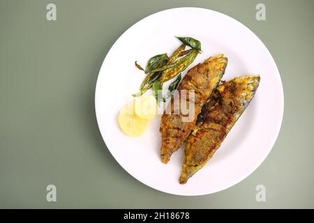 Indische Makrelenfischbraten. Bangda Rava Fry. Gebratener Fisch auf einem Bananenblatt mit gebratenen Chilischoten, Zitronenscheiben und indischen Gewürzen. Stockfoto