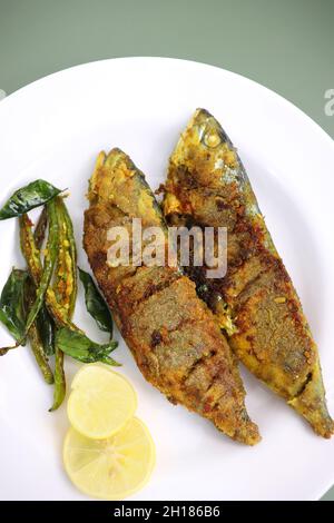 Indische Makrelenfischbraten. Bangda Rava Fry. Gebratener Fisch auf einem Bananenblatt mit gebratenen Chilischoten, Zitronenscheiben und indischen Gewürzen. Stockfoto