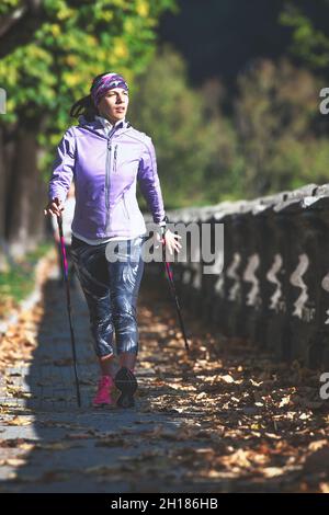 Nordic Walking auf dem Bürgersteig. Eine junge Frau praktiziert es und entspannt sich nach einem Arbeitstag Stockfoto