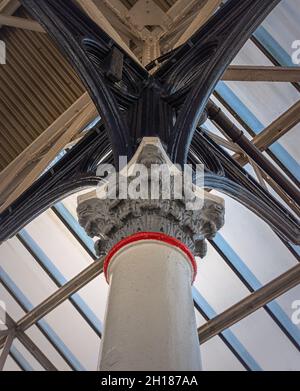 Blick nach oben auf eine historische korinthische Säule aus dem 19. Jahrhundert, die einen Baldachin stützt. Ein Oberlicht wirft Licht auf ein kompliziertes Eisenwerk. Stockfoto